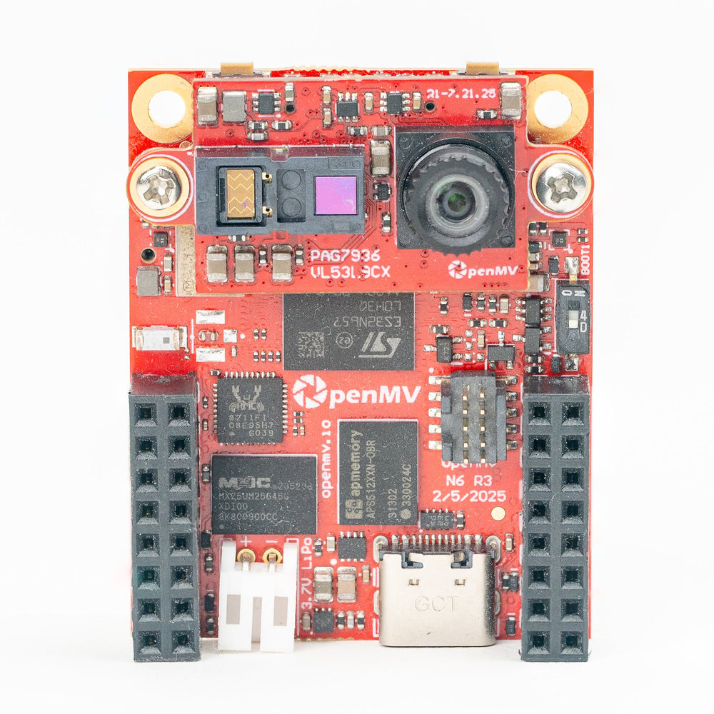 An OpenMV industrial vision board with a red printed circuit board, black pin headers, a camera lens, and various electronic components, photographed on a clean white background.