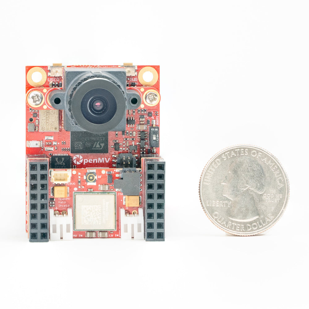 A small red electronic circuit board with a camera lens and connectors, shown next to a US quarter coin for scale, on a white background.