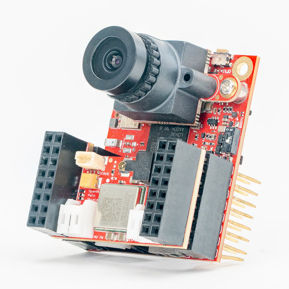 A compact electronic camera module with a black lens, red circuit board, and gold pins, photographed on a clean white background.